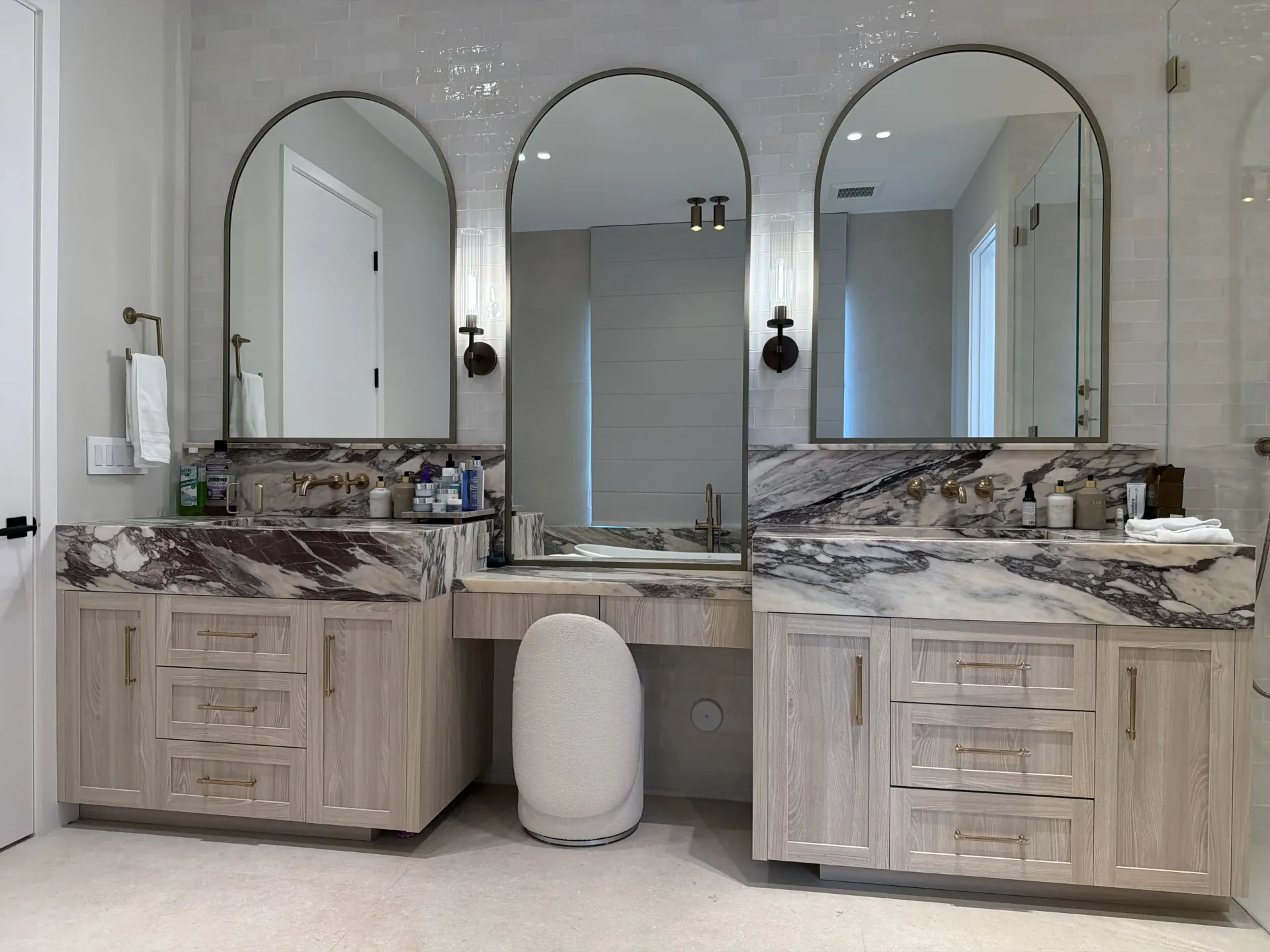 Double-vanity bathroom with light wood cabinetry and three arched mirrors