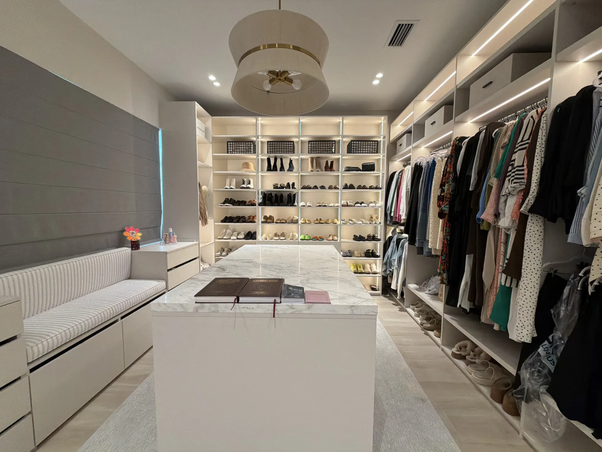 Walk-in closet with white built-in wardrobes, a center island, lit shoe shelving, and a window bench